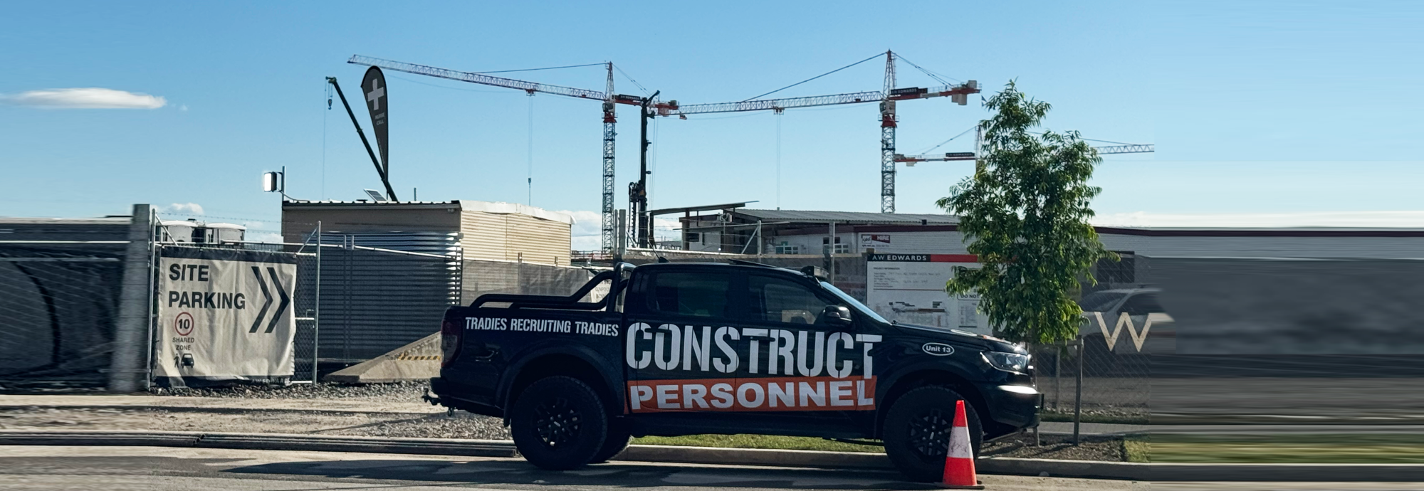 Branded Construct Personnel company vehicle parked at a construction site with cranes in the background.
